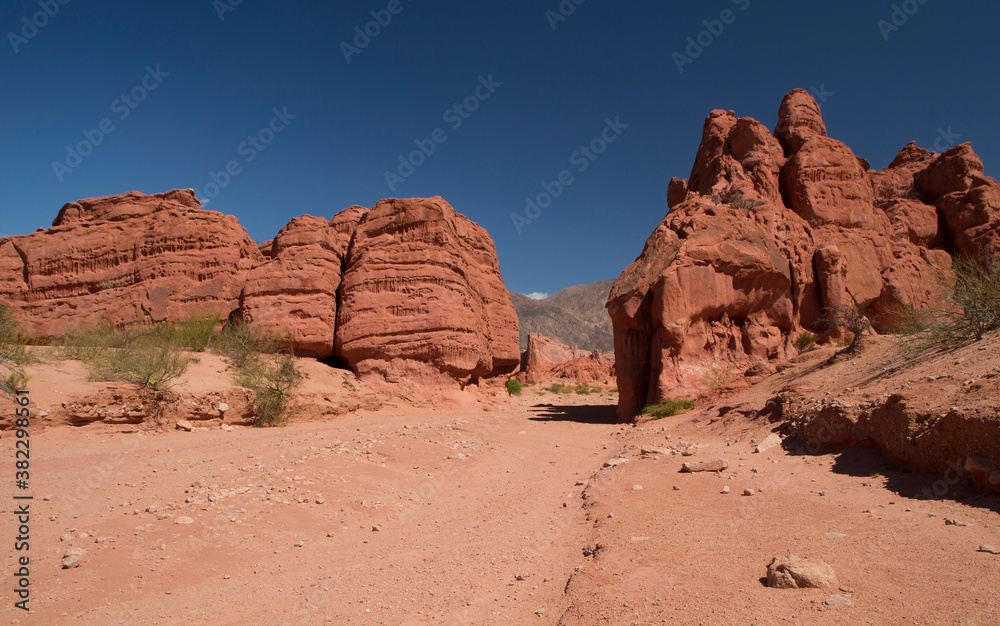 Desert landscape. Red canyon. View of the natural hiking path along the sand, rock and sandstone formations and mountains under a deep blue sky. 