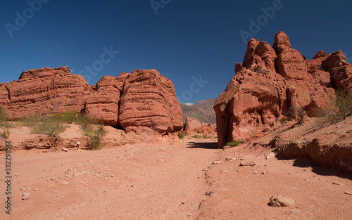 Desert landscape. Red canyon. View of the natural hiking path along the sand, rock and sandstone formations and mountains under a deep blue sky. 