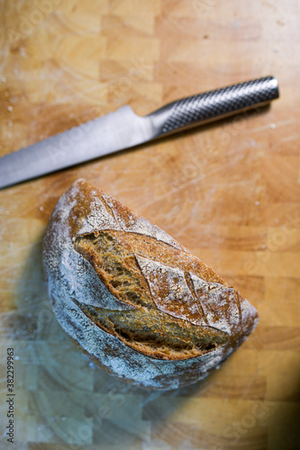 Overhead view of part of a homemade sourdough bread on a wooden cutting board with a serrated bread knife