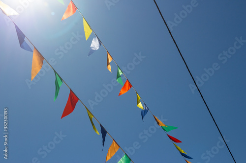 Colored flags stretched in the air against a blue sky. Festive street decoration 