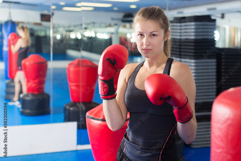 Portrait of young serious woman boxer who is training in gym.