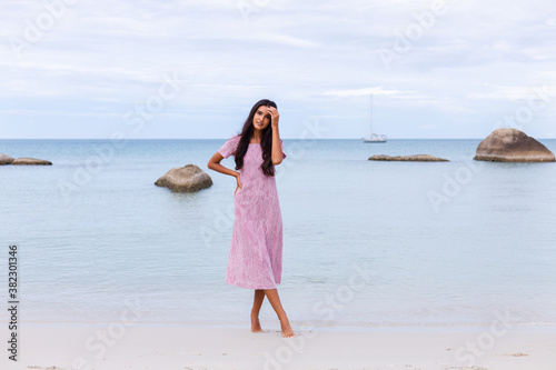 Young romantic girl with long dark hair in dress on the beach, smiling and laughing, having a nice time alone. 