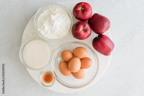 Eggs, sugar, flour, vanilla, and apples close up on marble board, directly from above, copy space. Ingredients for baking needs