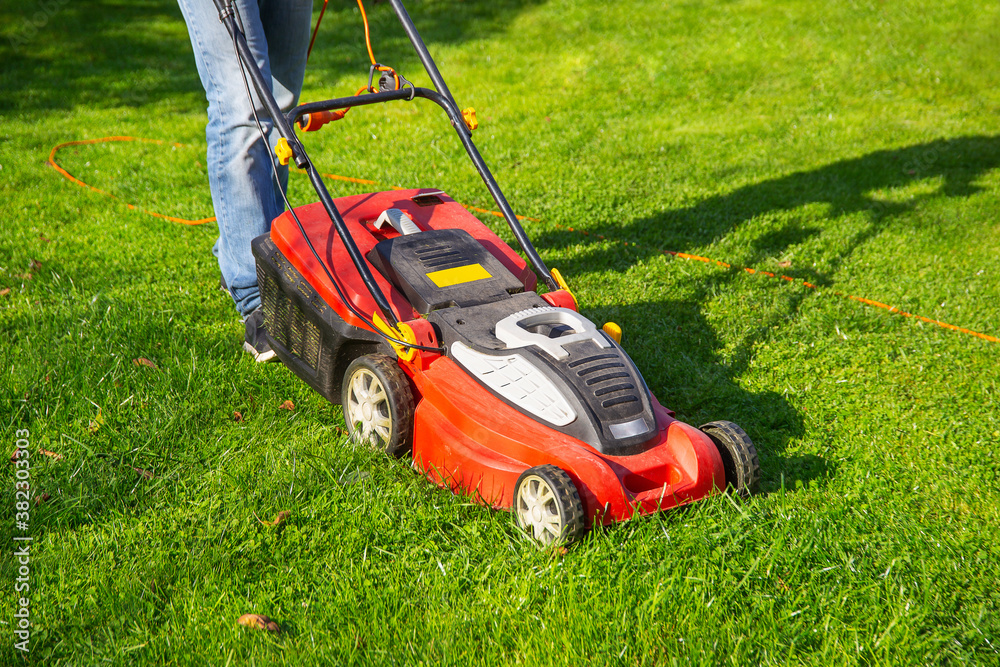 a man in jeans mows the grass in the garden with a lawn mower, summer day a man in jeans mows the grass in the garden with a lawn mower, summer day
