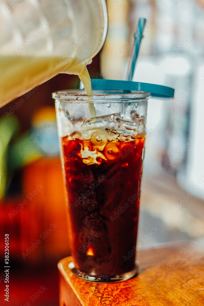 Iced coffee in a tall glass on a wood table with cream poured over Iced coffee in a tall glass on a wood table with cream poured over