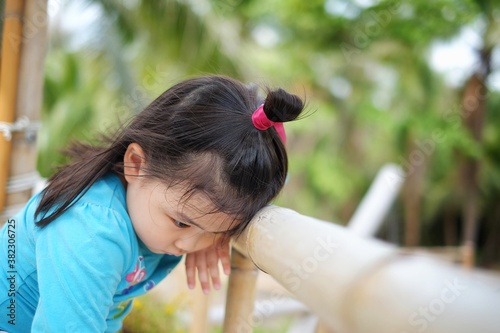 A cute young Asian girl feeling tired and bored, resting her head on her arm against a wooden rail.