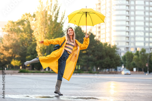 Beautiful young woman with umbrella wearing raincoat outdoors photo