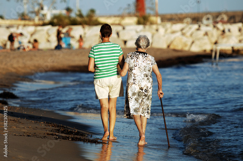 A middle aged woman walks arm in arm with her elderly mother in the coastal waters at the beach of Villajoyosa-Spain. photo