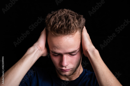 dramatic  portrait of sad embarrassed pensive teenager / young guy. Young man, unshaven, with a beard holding his head