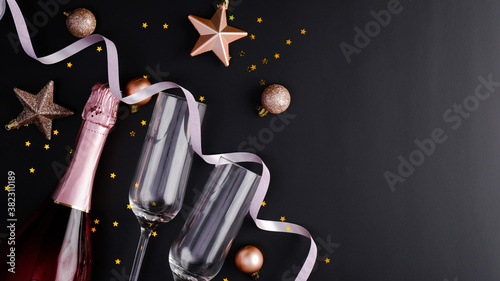 Elegant Christmas composition with rose wine bottle, champagne glasses, balls decorations, stars, confetti on black background. Flat lay, top view. Christmas or New Year Eve celebration concept.