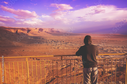 Young man standing on a viewpoint on the mount  Masada  and gazing sunrise in the desert. The man looking at the valley. Dead sea region  Masada  Israel