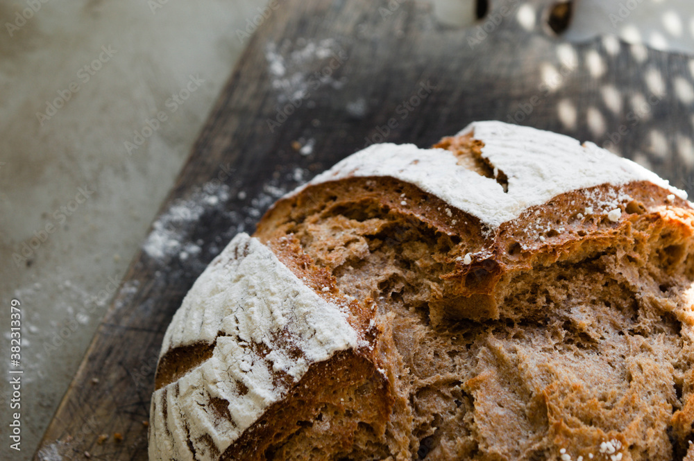 Fototapeta premium Half of homemade whole grain wheat and rye bread dusted with flour on the vintage wooden pan