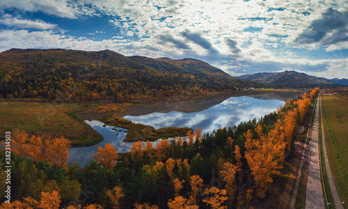 Aerial view of road and lake in beautiful autumn Altai forest. Beautiful landscape with empty rural road  golden autumn in altai  trees with red  yellow and orange leaves.
