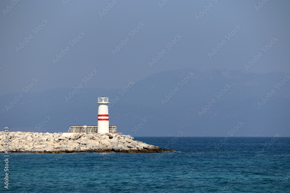 Lighthouse tower on a stone pier in azure sea against misty mountains