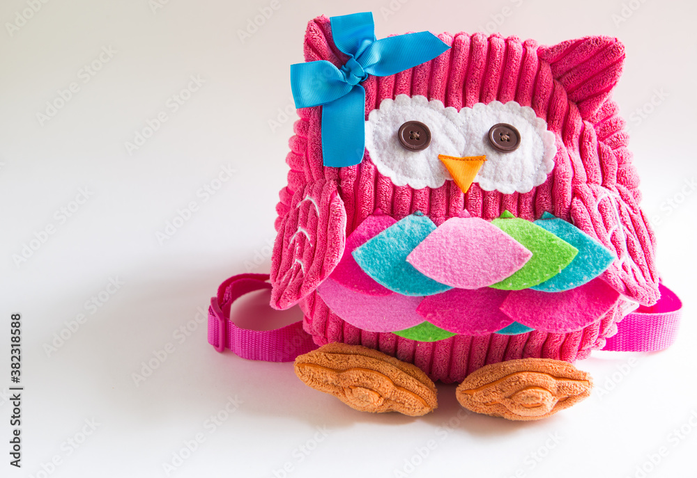 Obraz premium Toy pink backpack for girls in the shape of an owl with eyes buttons, applique, ribbon and embroidery. Handmade, DIY with children. Gray background