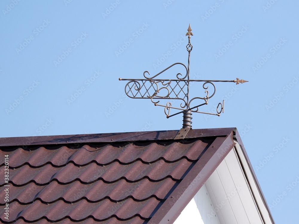 Weather vane on the roof of the house. Part of the image is blurred. Weather vane on the roof of the house. Part of the image is blurred.