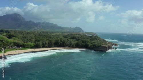 Poipu beach in aerial drone clip. Blue sky summer time tropical coastline. Vacation paradise at Shipwrecks Beach close to Grand Hyatt Resort in Kauai, Hawaii. Surfer waiting in water to catch waves photo