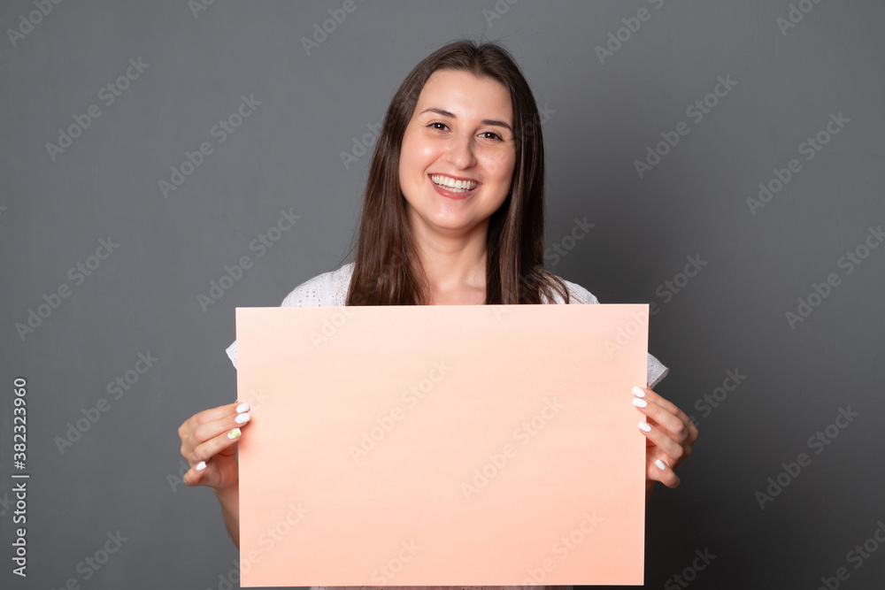 Happy young woman holding a blank banner. Smiling brunette woman holding blank sheet of paper for text.