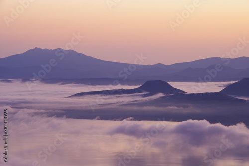 湖を覆う朝靄と山々のシルエット。北海道、津別峠からの夜明けの風景。