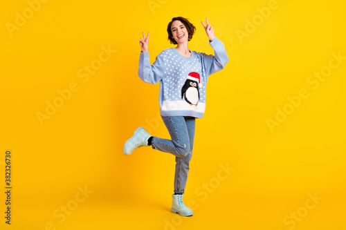 Full length photo of attractive cute lady x-mas party good mood greet friends show v-sign symbol wear penguin ugly ornament sweater jeans shoes isolated yellow shine color background © deagreez