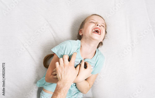 Foto Family time: a little girl lies on the bed and laughs cheerfully because of the tickling of her father