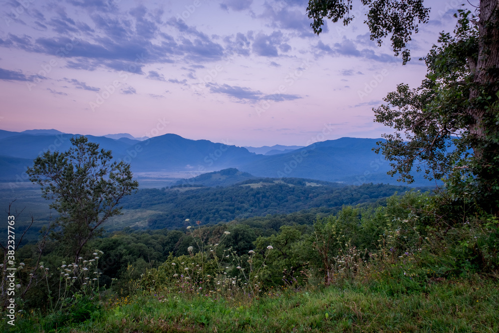 Early morning one hour before dawn. Silhouettes of mountains in the morning haze, grass and trees in the foreground. Lagonaki Plateau, Republic of Adygea, Russia