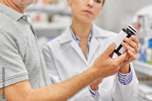medicine, pharmaceutics, healthcare and people concept - pharmacist showing drug to senior man customer at drugstore