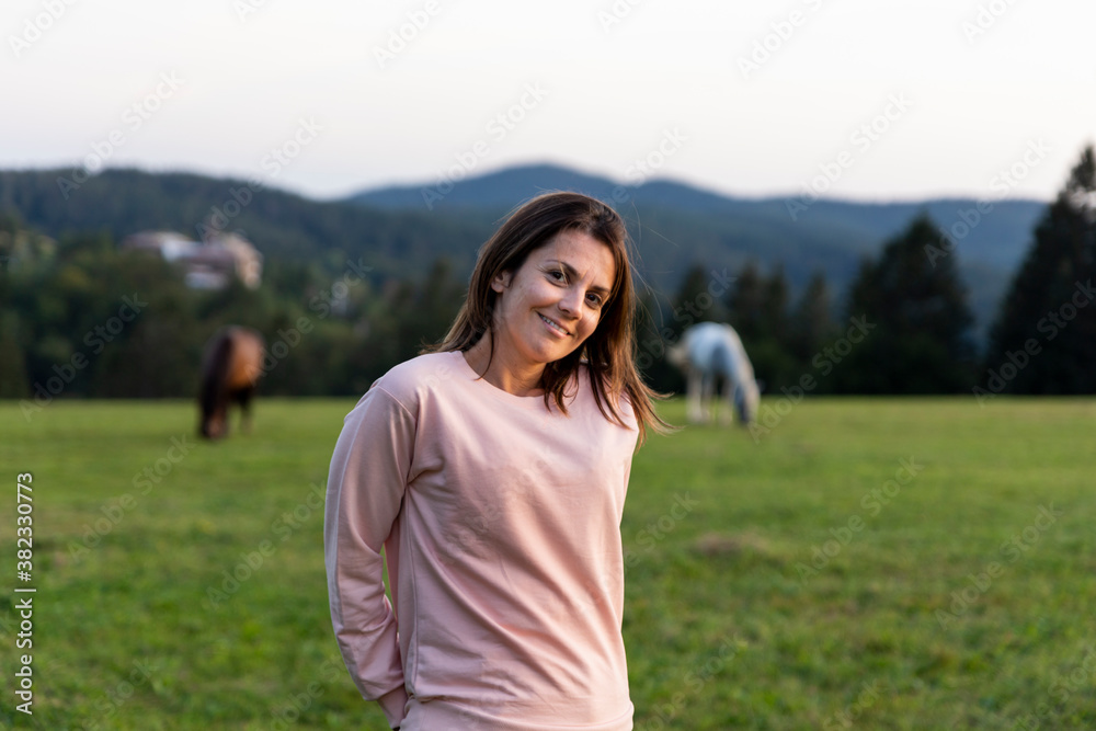 Beautiful woman at horse farm with horses in the background at sunset Beautiful woman at horse farm with horses in the background at sunset