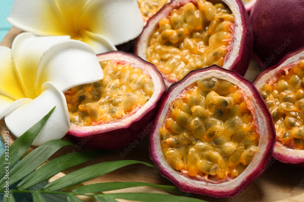 Halves of passion fruits (maracuyas), palm leaf and flowers on wooden plate, closeup