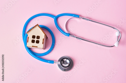 Medical stethoscope and toy house on a pink background with copy space