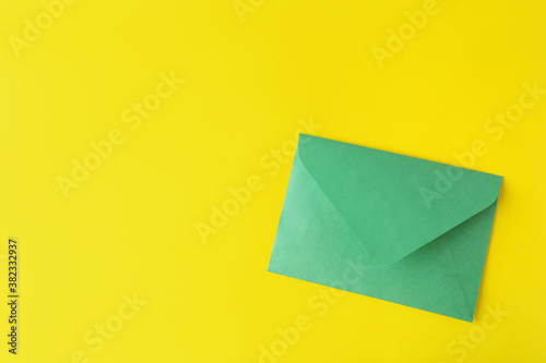 Green paper envelope on yellow background, top view. Space for text
