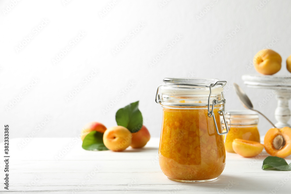 Jar of apricot jam and fresh fruits on white wooden table. Space for text Jar of apricot jam and fresh fruits on white wooden table. Space for text