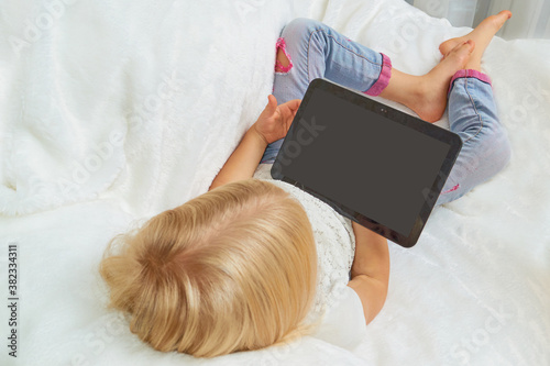 A girl lies on an armchair with a white pedal and holds a tablet in her hands, homeschooling on vacation and quarantine