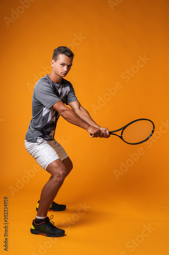 Full-length portrait of a tennis player man in action against orange background