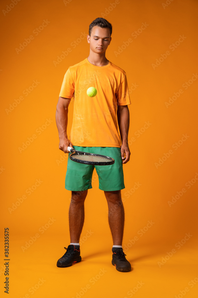 Full-length portrait of a tennis player man in action against orange background Full-length portrait of a tennis player man in action against orange background