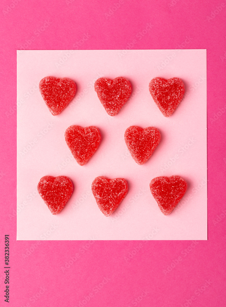 Fototapeta premium Many sugar coated pink candy hearts arranged in rows on pink background in studio setting
