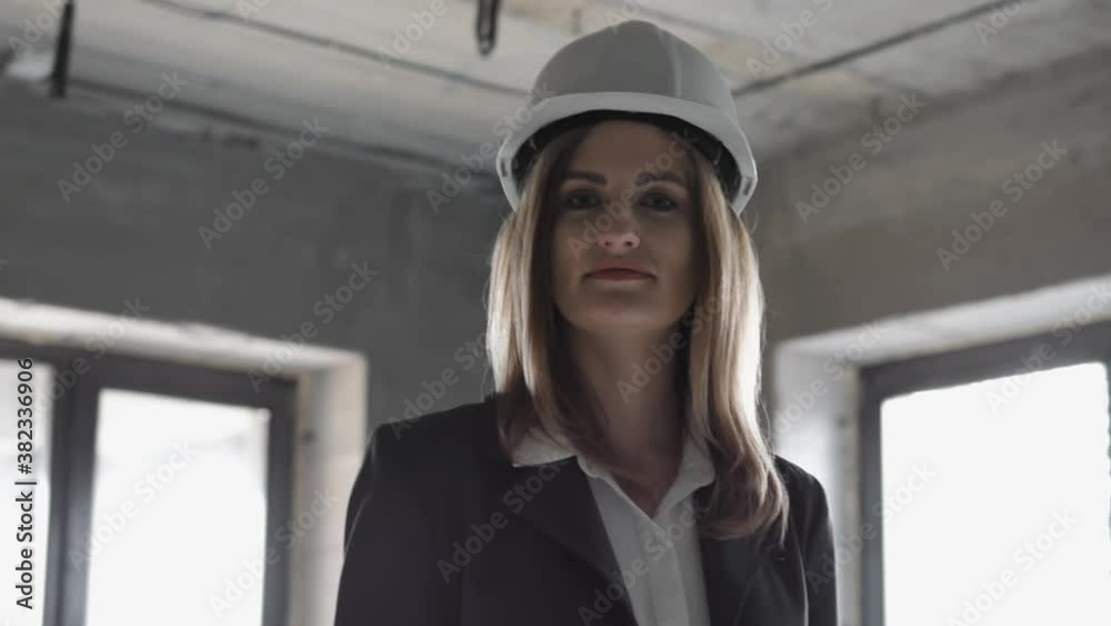 Portrait of pretty hard working young woman engineer specialist or worker in a uniform and protective white helmet, smiling and looking at camera at construction site Portrait of pretty hard working young woman engineer specialist or worker in a uniform and protective white helmet, smiling and looking at camera at construction site