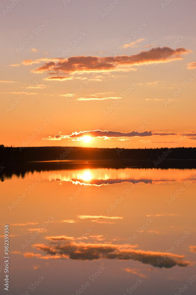 Sunset with strong colors. Lake, horizon, orange sky with cloudlets, glowing sun and reflection. Kemijärvi Finland.