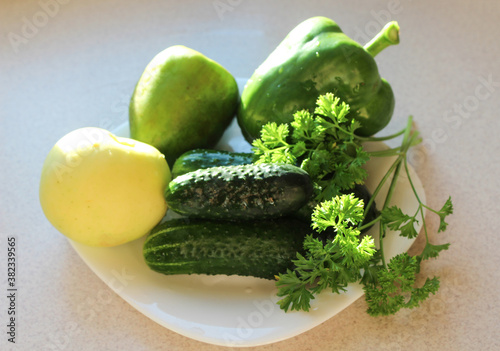 Fresh vegetables and fruits - Apple, cucumber, pepper, parsley - on a white saucer on a gray kitchen table, close - up-the concept of proper healthy nutrition
