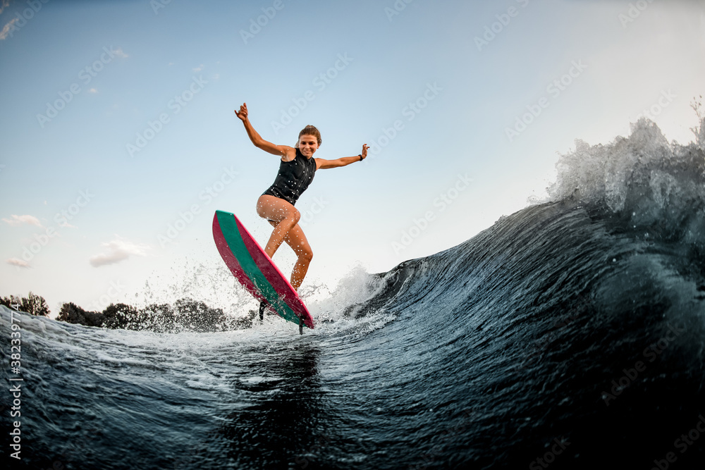 cheerful woman stands on bright surf style wakeboard and jumps over water