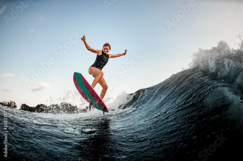 cheerful woman stands on bright surf style wakeboard and jumps over water