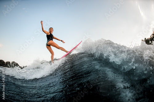 side view of woman balanced on surf style wakeboard on splashed river wave
