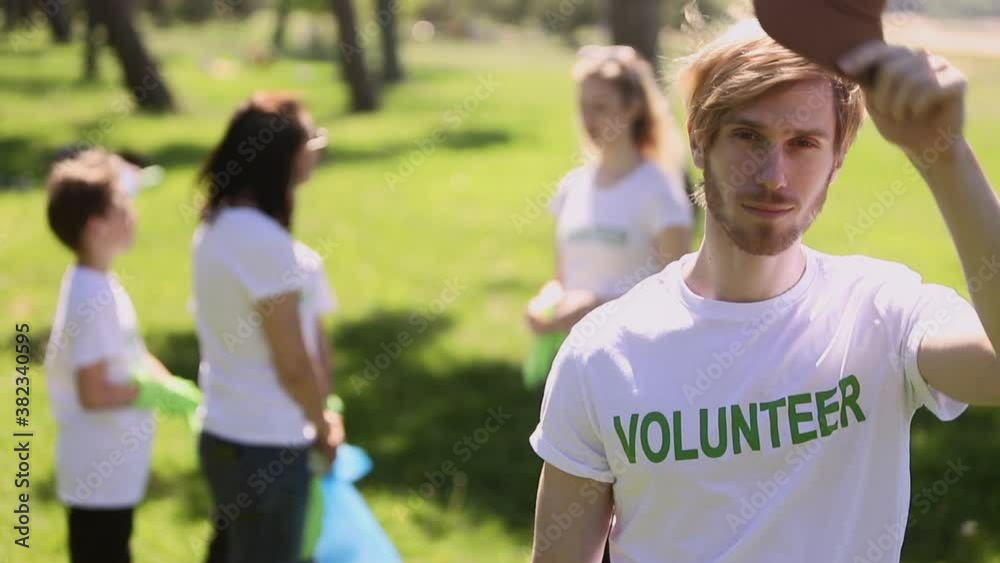 Male volunteer family recycle plastic bottle posing with smile while standing in green park during ecological cleaning spbi. Handsome guy looking forward and smiling, taking off cap from his head