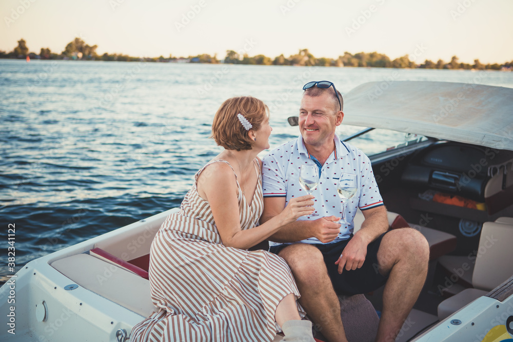 Beautiful couple man and woman drink wine while sitting in a boat. Romantic relationship.