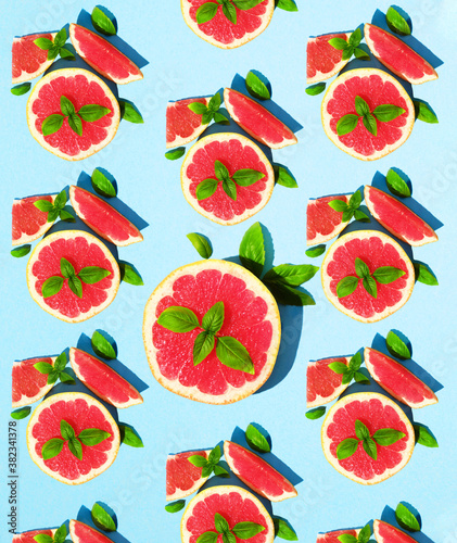 Fototapeta Naklejka Na Ścianę i Meble -  Concept lots of juicy slices of grapefruit and green Basil on a bright blue paper background. Pattern