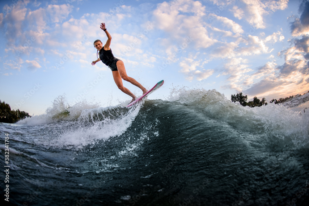 Active girl in swimsuit jumping up on surf style wakeboard against blue cloudy sky