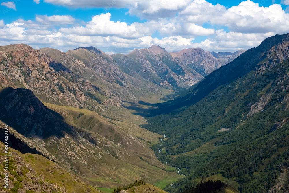 Naklejka premium Mountain gorge landscape with cloudy blue sky. Summer nature landscape. River valley panorama. Kora river gorge in Kazakhstan, way to Burkhan bulak waterfall. Tourism in Kazakhstan concept.