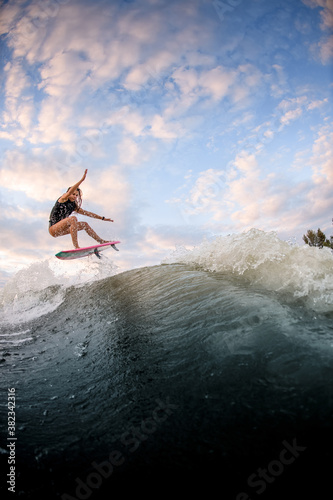 beautiful view of woman jumping over big splashing wave on surf style wakeboard.