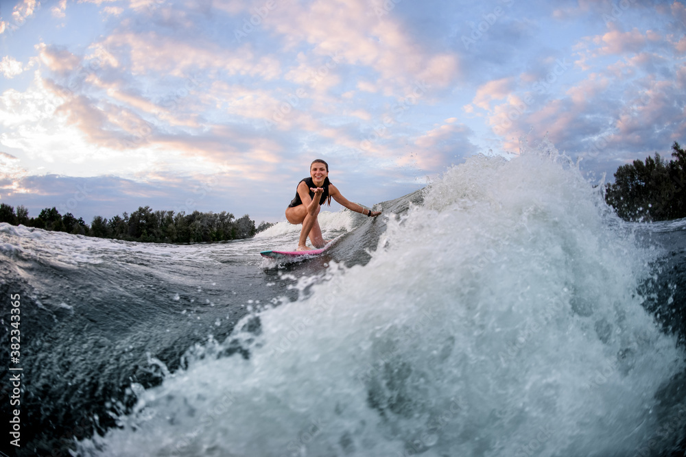 Active woman rides wave on surf style wakeboard and touches wave with hand