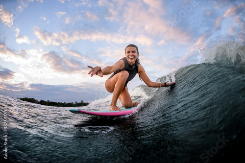 happy young woman rides wave on surf style wakeboard and touches wave with hand